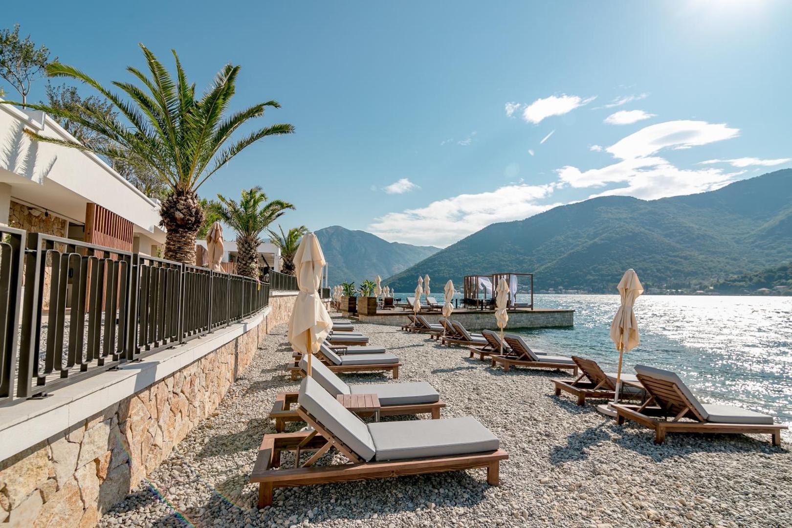 Boutique Hotel & Spa Casa del Mare oļu pludmale Melnkalnē ar sauļošanās krēsliem, saulessargiem un skatu uz Kotoras līča kalniem
