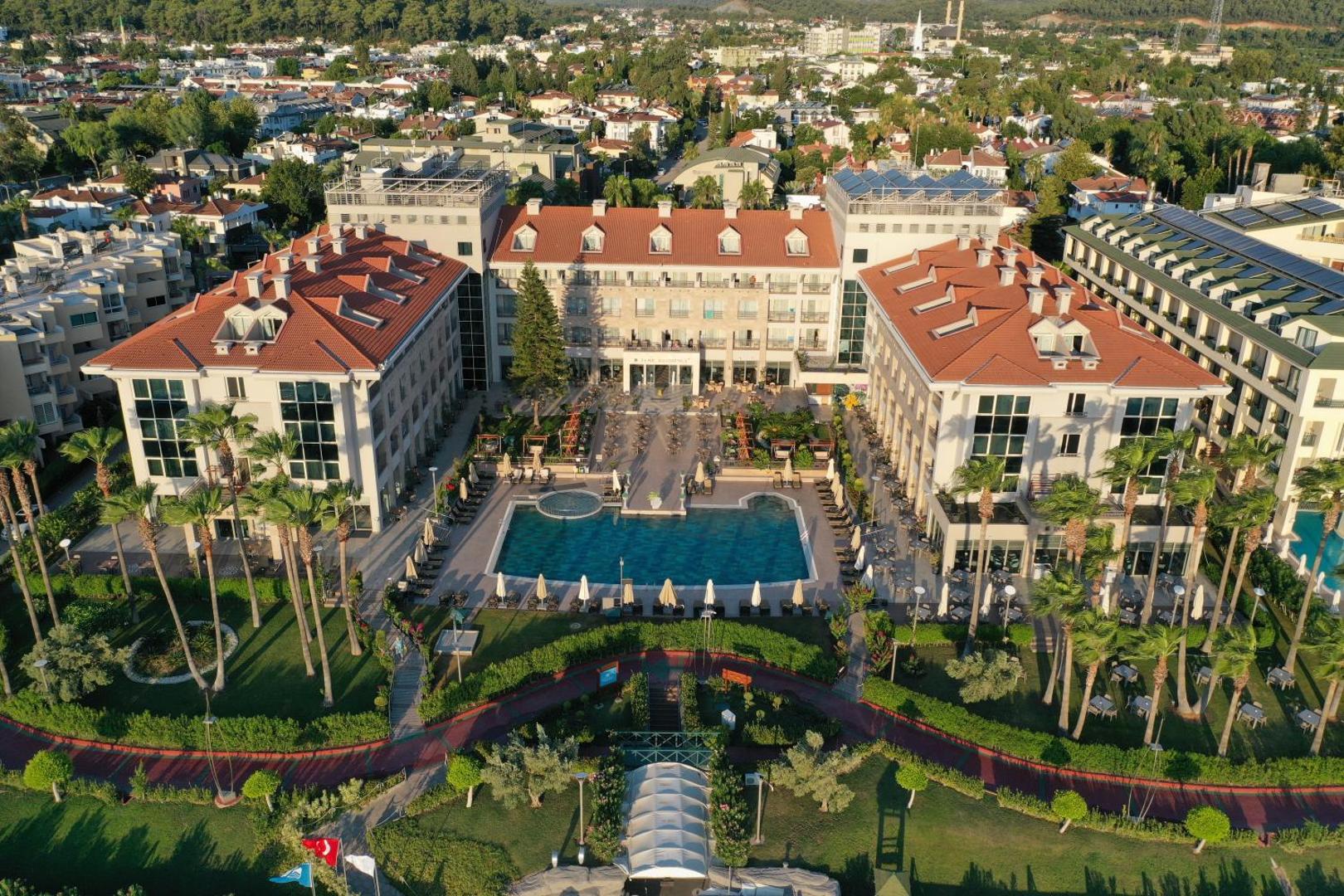 Fame Residence Kemer & Spa aerofoto skats uz viesnīcas iekšpagalmu ar āra baseinu, sauļošanās krēsliem un apkārtējo pilsētas ainavu