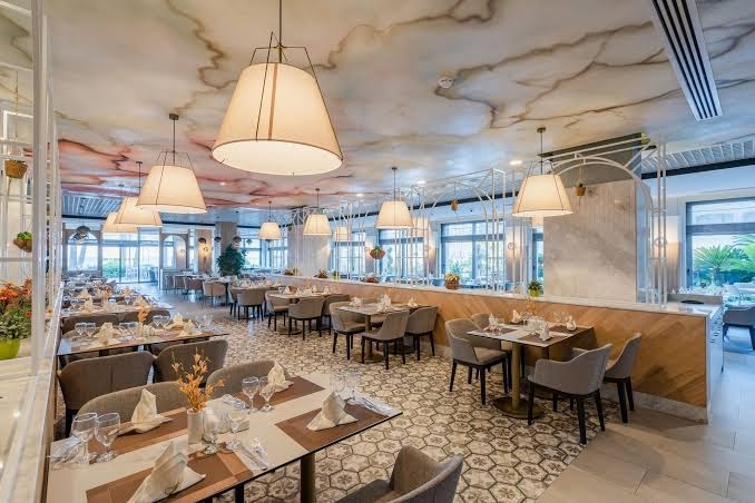 Fame Residence Kemer & Spa galvenais restorāns ar modernu interjeru, dekoratīviem griestiem un eleganti klātiem galdiem Kemeras kūrortā Turcijā