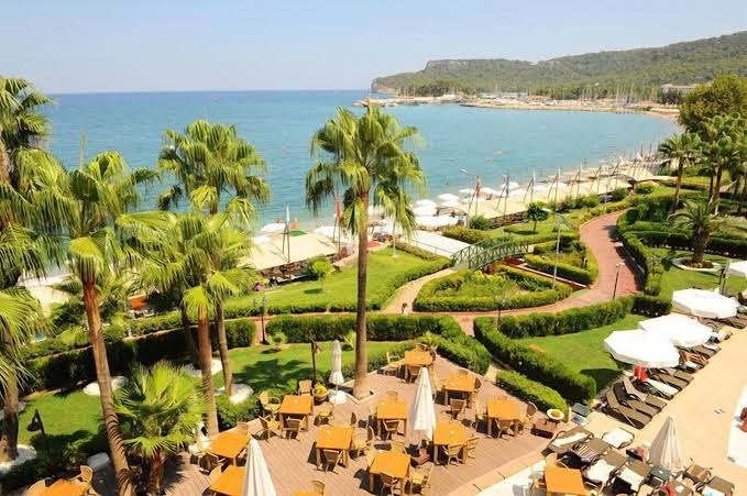 Fame Residence Kemer & Spa skats no augšas uz dārzu, āra terasi ar galdiņiem un Vidusjūras piekrasti Kemeras kūrortā