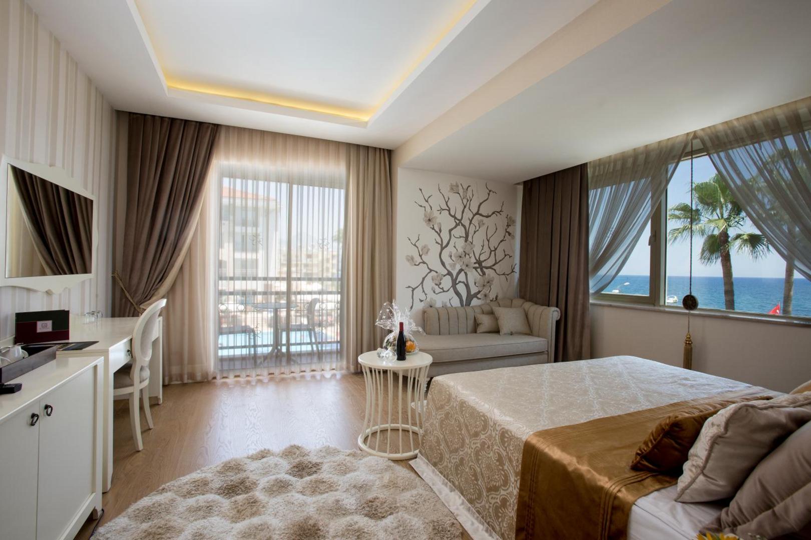 Gaišs Fame Residence Kemer & Spa numurs ar dekoratīvu sienas zīmējumu, atpūtas dīvānu un skatu uz pludmali un palmām