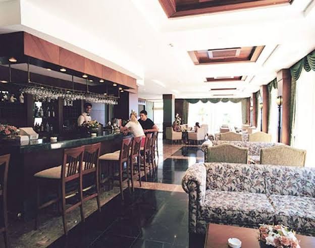 Fame Residence Kemer & Spa klasiskā stila bārs ar tumša koka apdari, mīkstajiem dīvāniem un bāra leti Kemeras viesnīcā