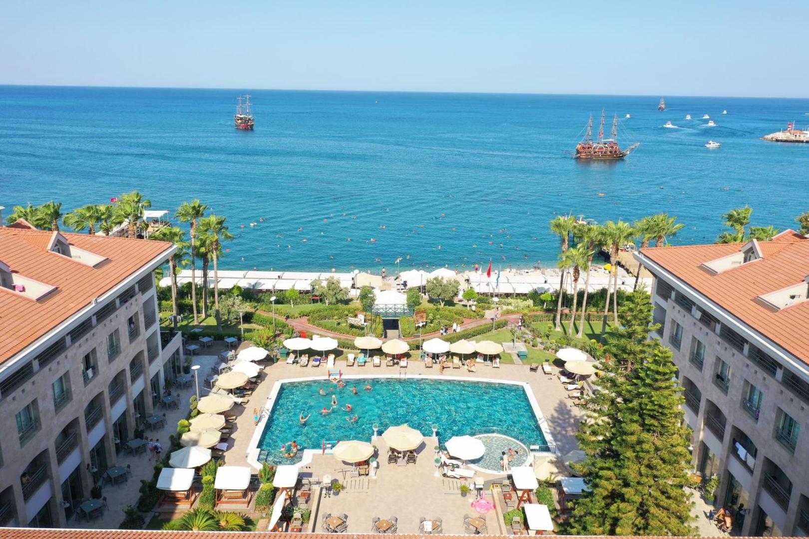 Aerofoto skats uz Fame Residence Kemer & Spa baseinu, pludmali un Vidusjūru ar kuģiem Kemeras piekrastē, Turcijā