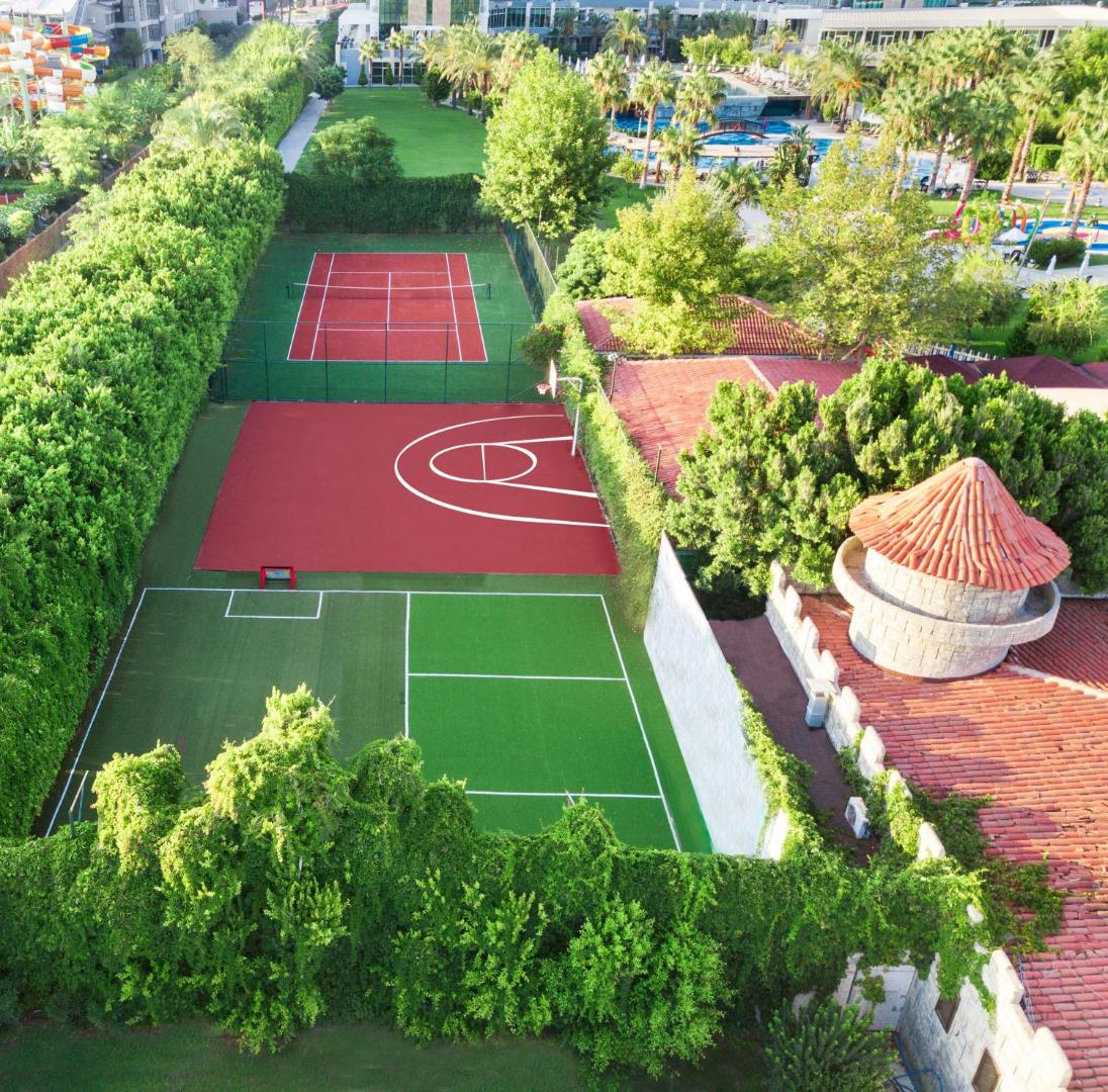 Sherwood Exclusive Lara sporta laukumi no putna lidojuma, redzams tenisa korts, basketbola laukums un futbola zona zaļumu ieskāvumā