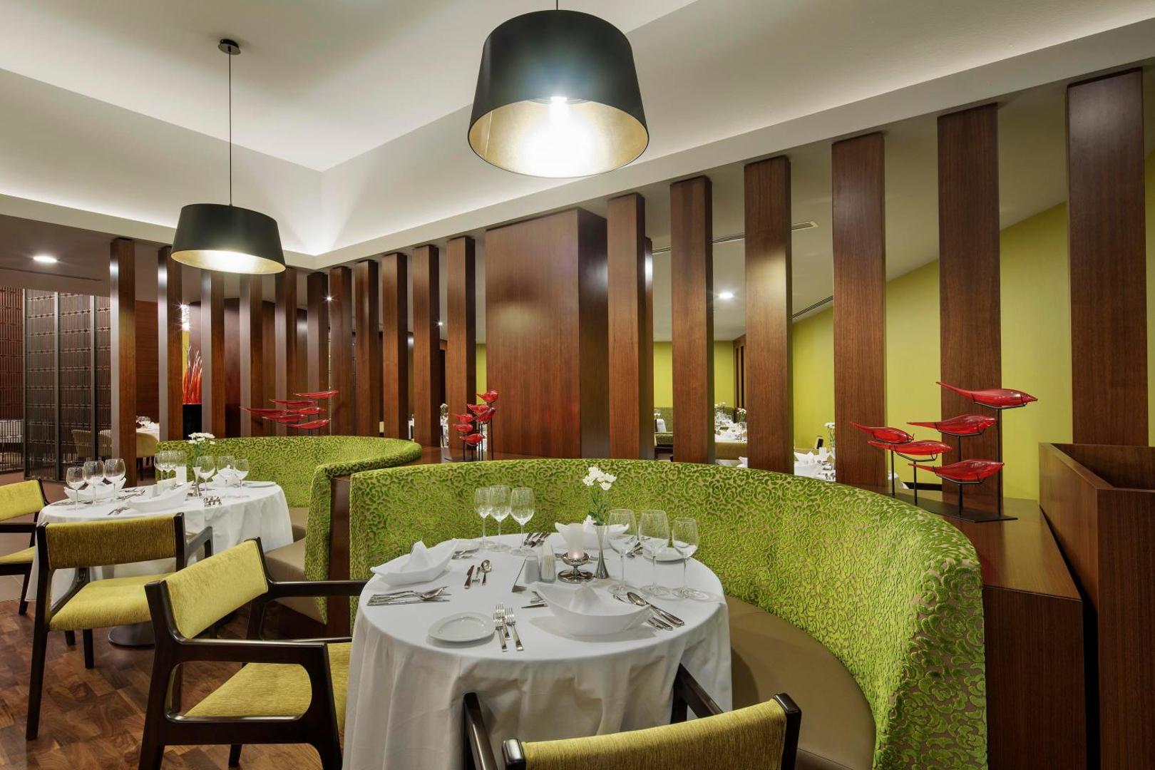 The Sense Deluxe a la carte restorāna zona ar zaļiem dīvāniem, koka apdari un modernu apgaismojumu mājīgai atmosfērai