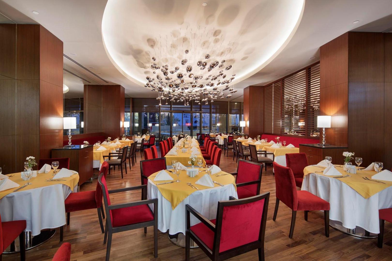 The Sense Deluxe elegantais iekštelpu restorāns ar sarkanu un dzeltenu krāsu akcentiem, greznu lustru un servētiem galdiem