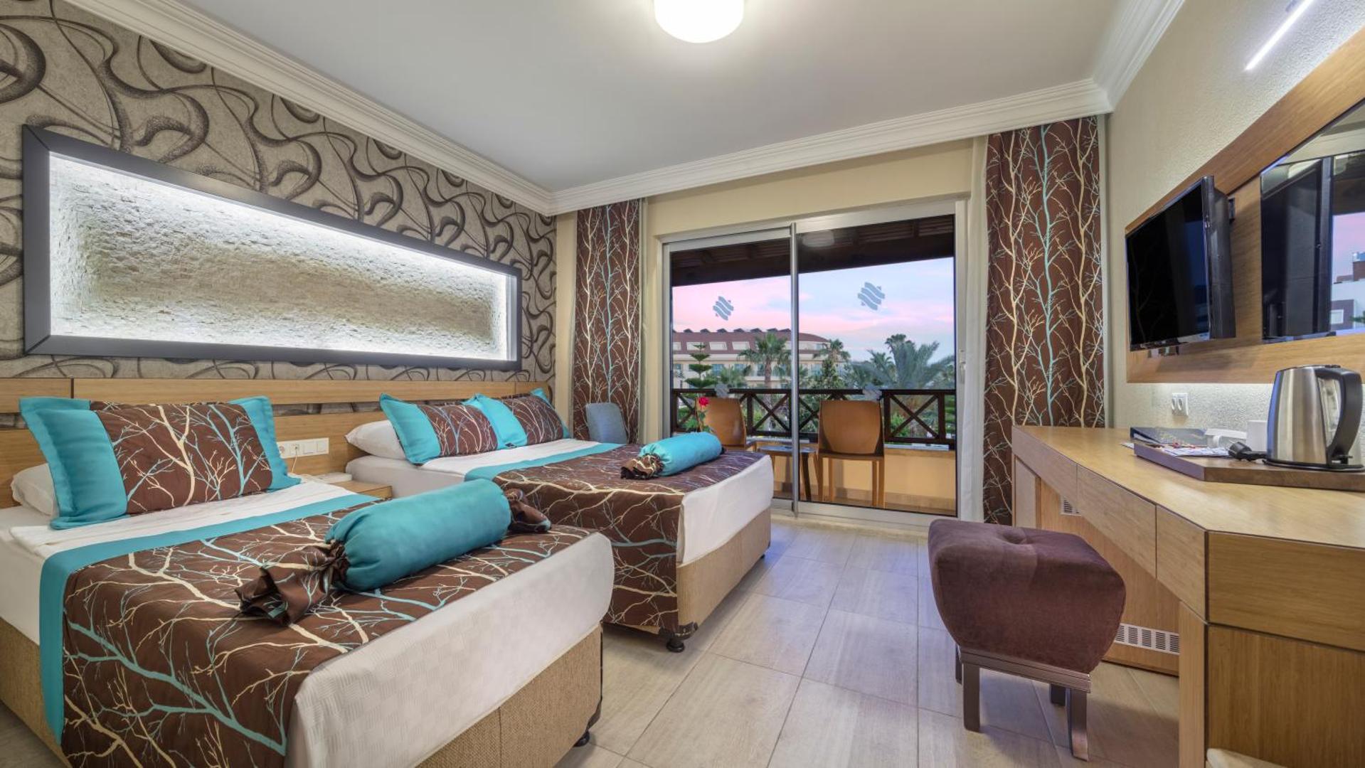 Saphir Hotel & Villas gaišs numurs ar divām gultām, koka mēbelēm un balkonu, no kura paveras skats uz kūrorta dārzu
