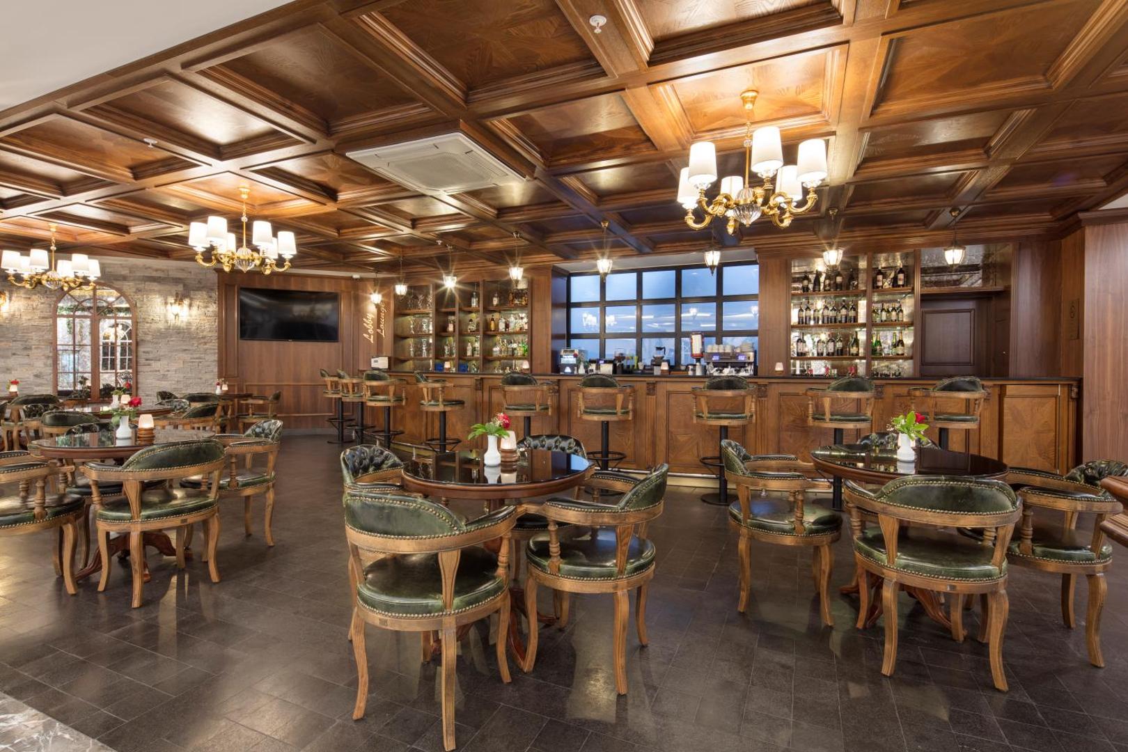 Saphir Hotel & Villas lobby bārs ar klasiskām koka mēbelēm, ādas krēsliem un greznām lustrām pie koka griestiem.