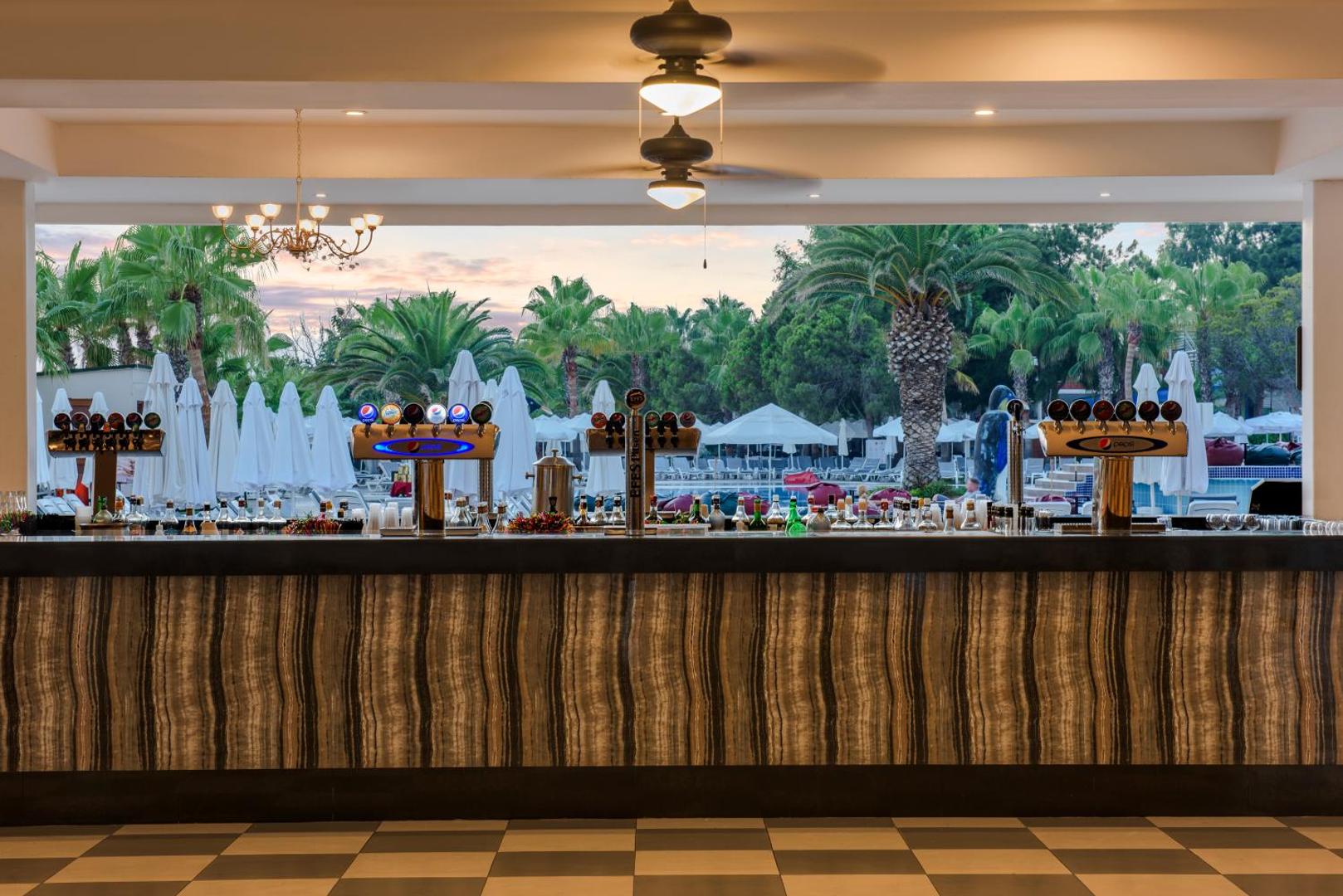 Botanik Hotel & Resort āra bārs ar skatu uz palmu dārzu un baseina zonu saulrieta laikā Alanjas reģionā
