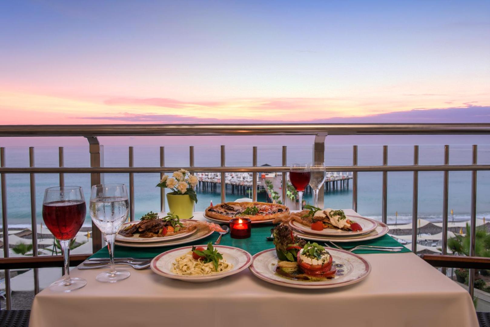Botanik Hotel & Resort restorāna galds uz balkona ar skatu uz jūru saulrietā — servēti ēdieni, vīns un sveces