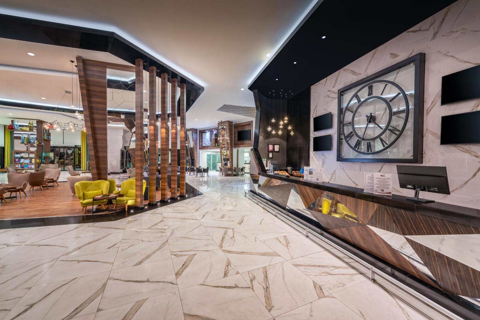 Botanik Hotel & Resort modernā recepcijas zona un lobby ar marmora grīdu, lielu sienas pulksteni un stilīgām atpūtas mēbelēm