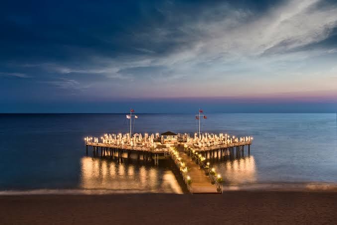 Botanik Hotel & Resort izgaismota koka piestātne jūrā vakara stundā — romantiska atmosfēra un atpūtas vietas uz ūdens