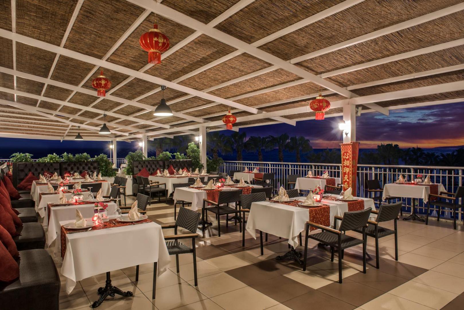 Botanik Hotel & Resort āra terases restorāns vakarā ar tradicionālām sarkanām laternām un skatu uz palmām un jūru