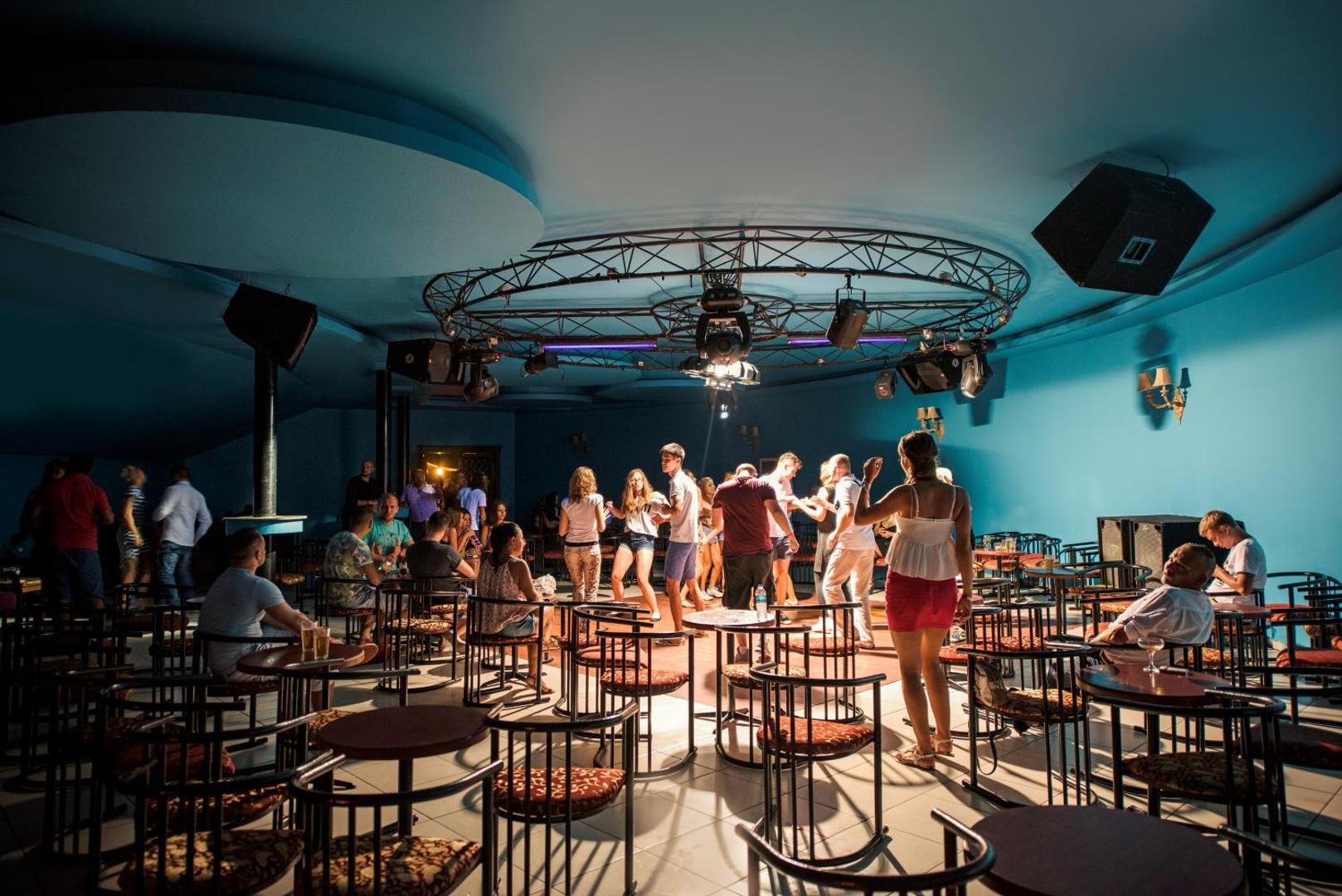Botanik Hotel & Resort nakts klubs ar dejotājiem uz skatuves, diskoballēm raksturīgu apgaismojumu un atpūtas zonu ar galdiņiem