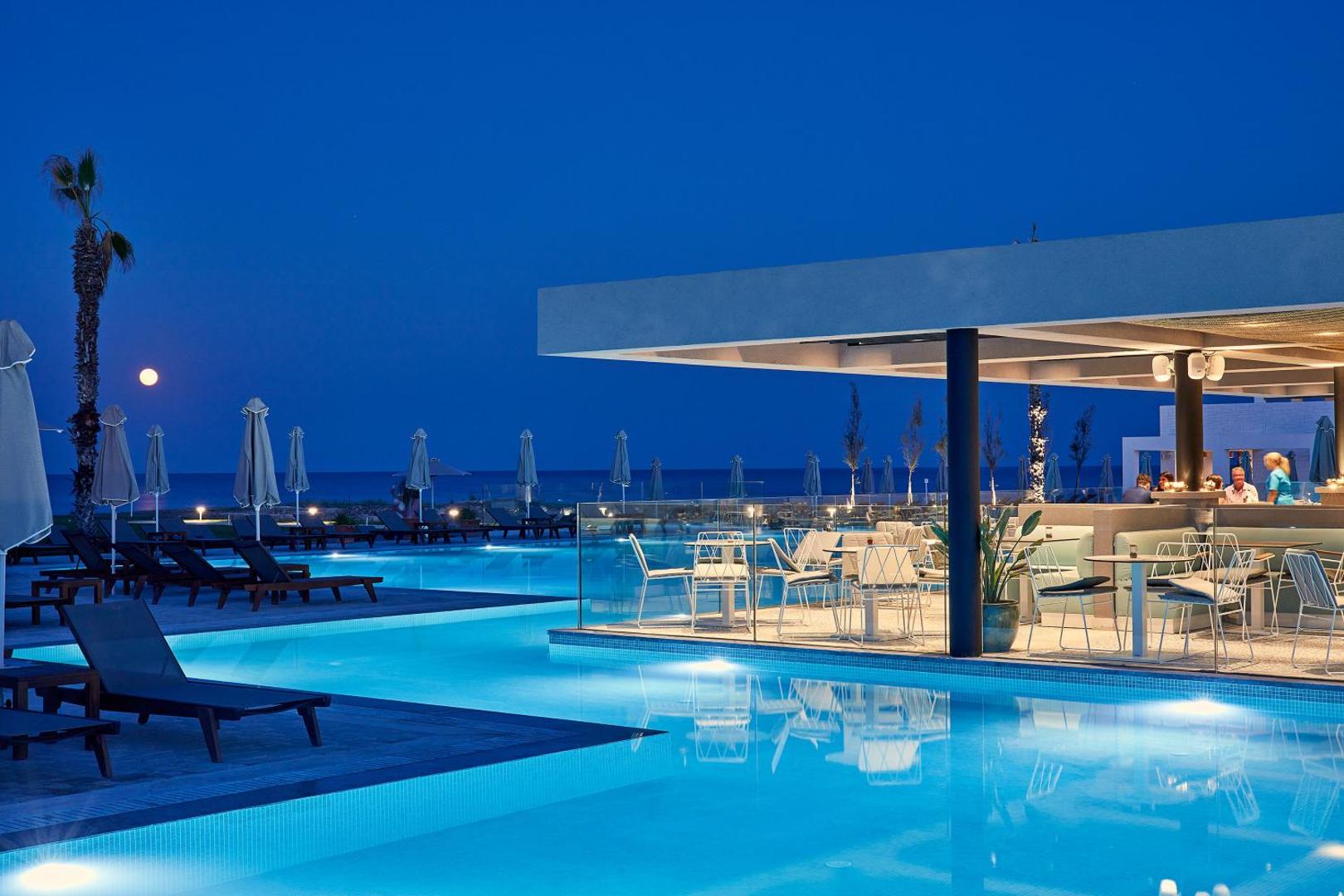 Atlantica Dreams Resort vakara skats uz baseinu un āra restorānu Rodā — izgaismota terase, bārs un jūra fonā