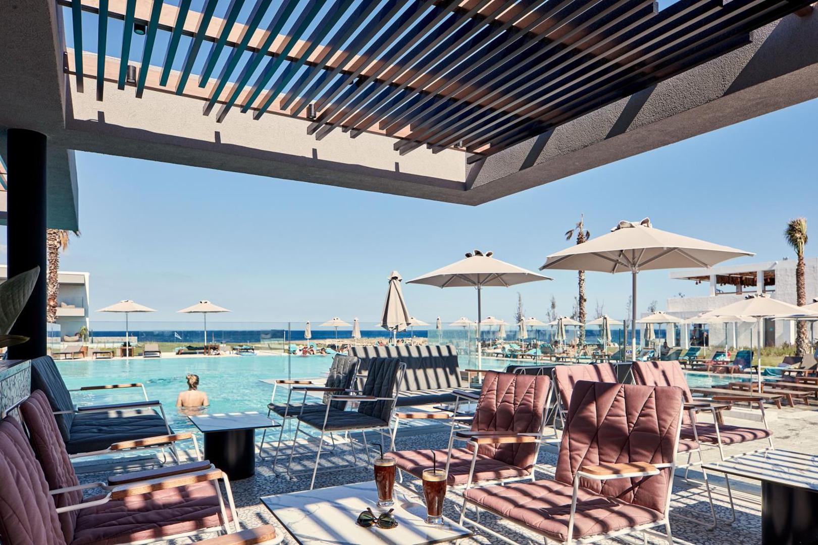 Atlantica Dreams Resort atpūtas zona pie baseina ar ērtiem krēsliem un saulessargiem Rodā — skats uz jūru no terases