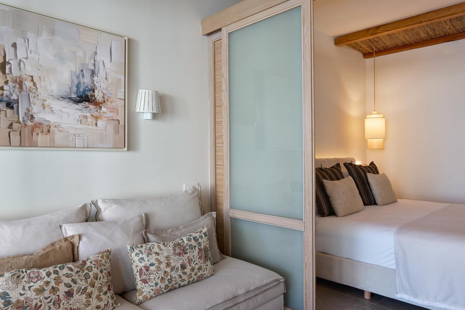Atlantica Dreams Resort gaišs numurs ar atpūtas zonu, dīvānu un bīdāmu stikla starpsienu, kas nodala guļamistabu.