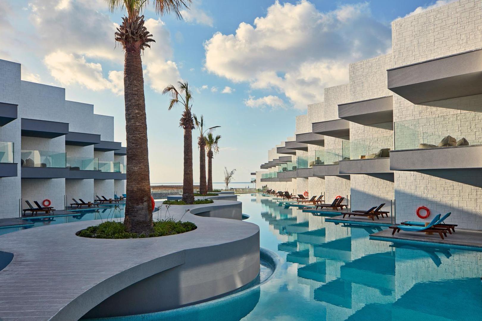 Atlantica Dreams Resort numuri ar tiešu piekļuvi baseinam Rodas salā — moderna arhitektūra, palmas un sauļošanās krēsli pie ūdens