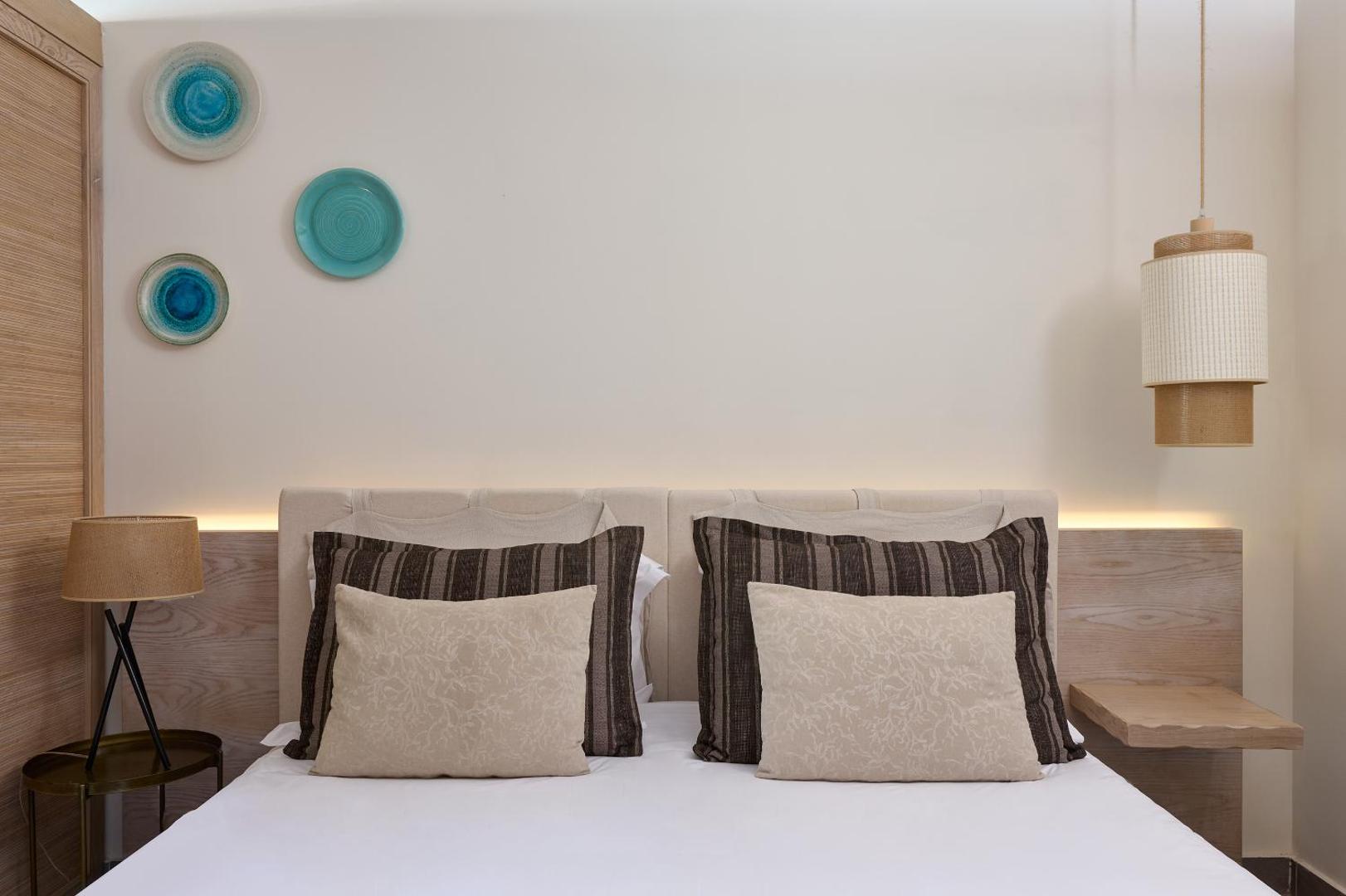 Atlantica Dreams Resort guļamistabas interjera detaļas ar dekoratīviem spilveniem, stilīgu lampu un koka elementiem pie sienas.