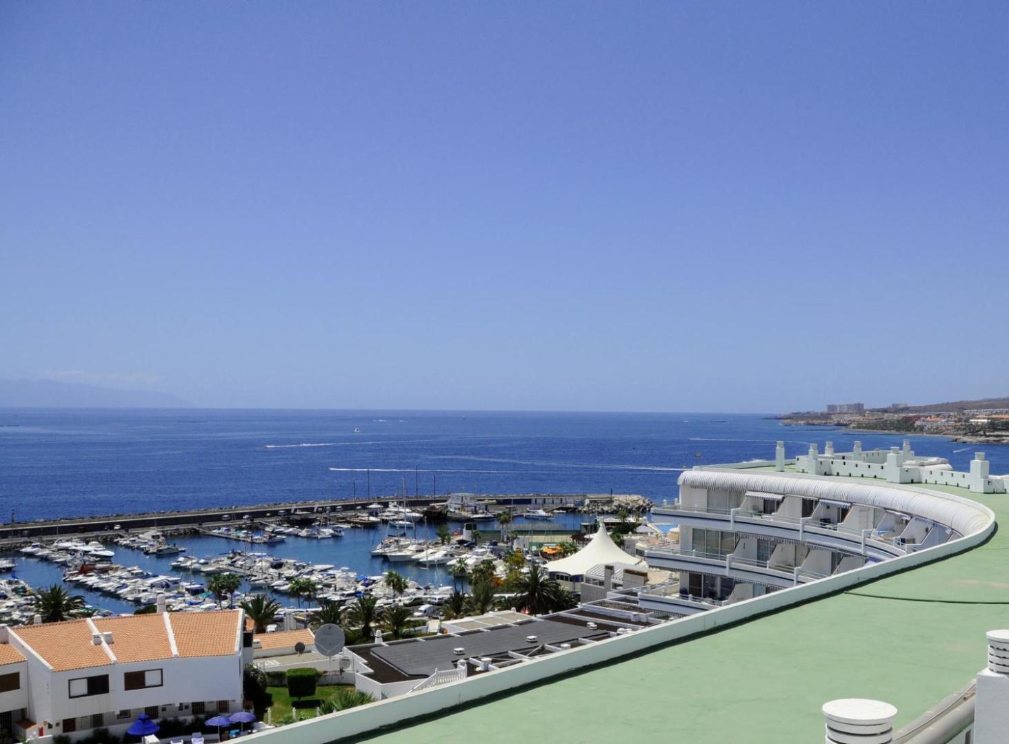Skats no Hovima Atlantis terases uz jahtu piestātni un zilo okeānu Tenerifē, redzama viesnīcas ēka ar balkoniem