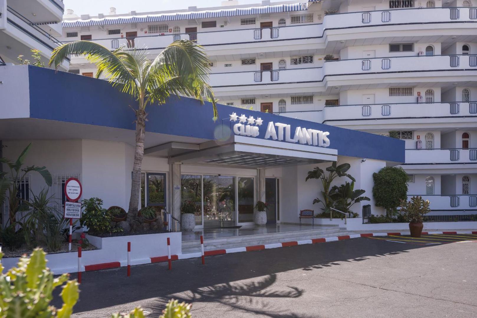 Hovima Atlantis četrzvaigžņu viesnīcas ieeja un fasāde — balta ēka ar ziliem akcentiem un palmu pie galvenajām durvīm