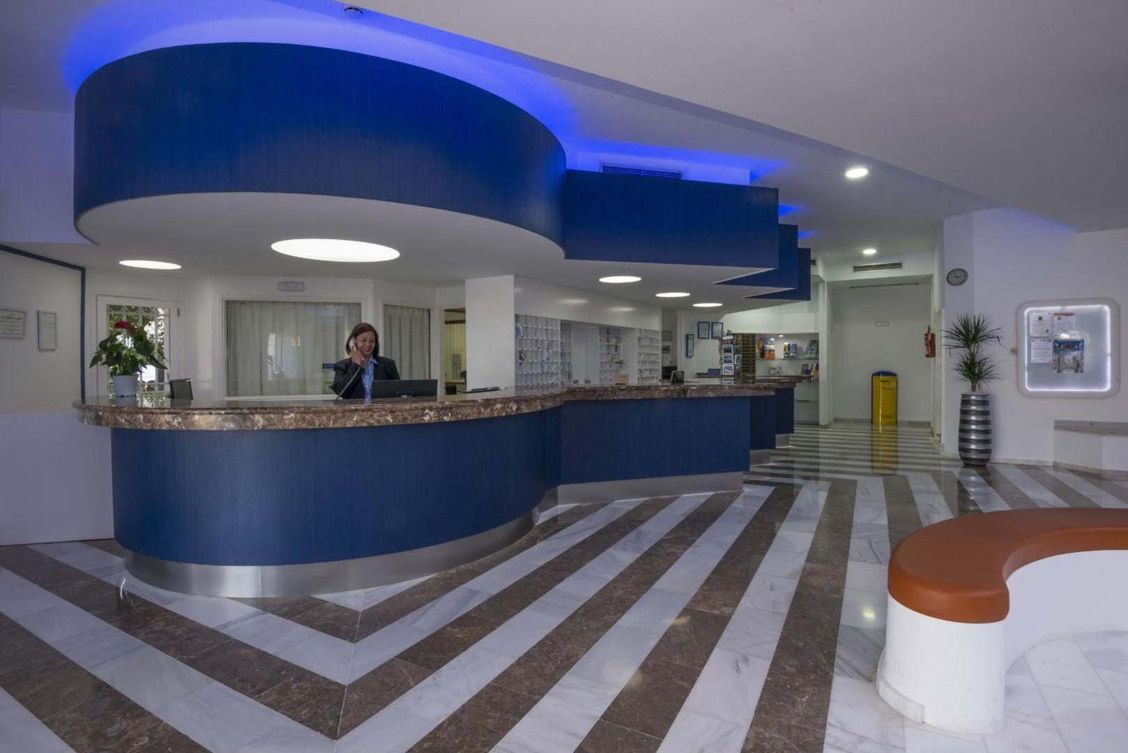Hovima Atlantis viesnīcas recepcijas zona ar modernu zilu leti, marmora grīdu un apgaismojumu viesu uzņemšanai