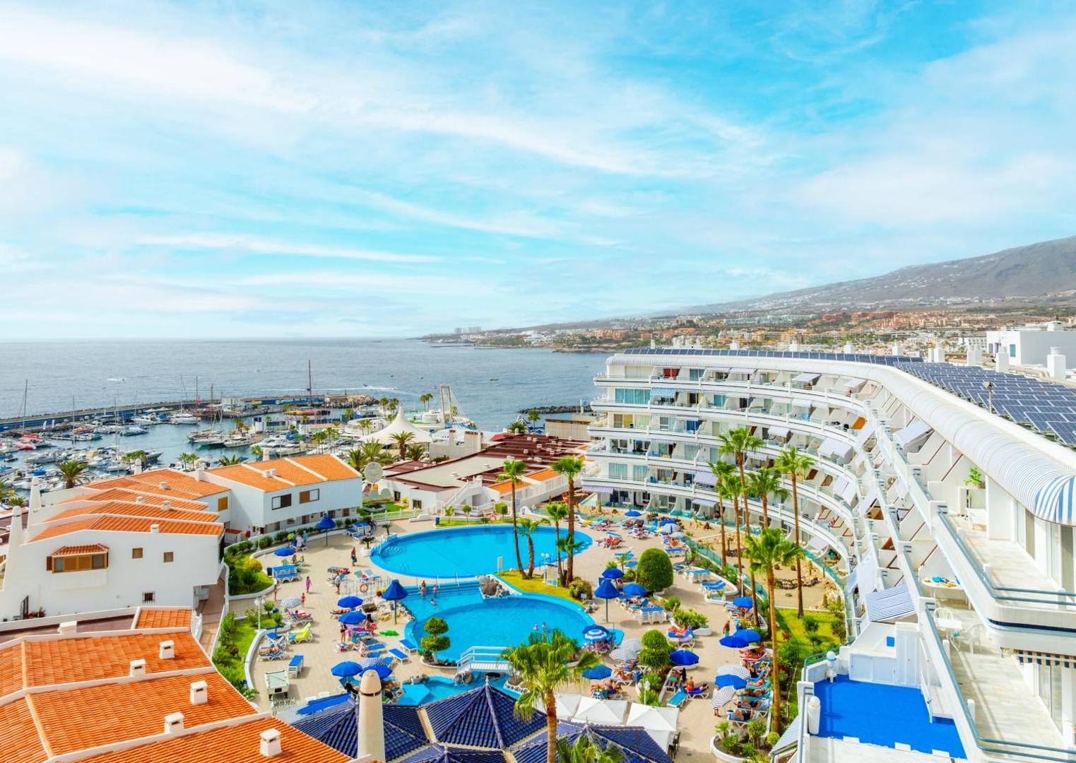 Hovima Atlantis viesnīcas kopskats ar baseiniem un jahtu piestātni Tenerifē — panorāmas skats uz okeānu un kūrorta teritoriju