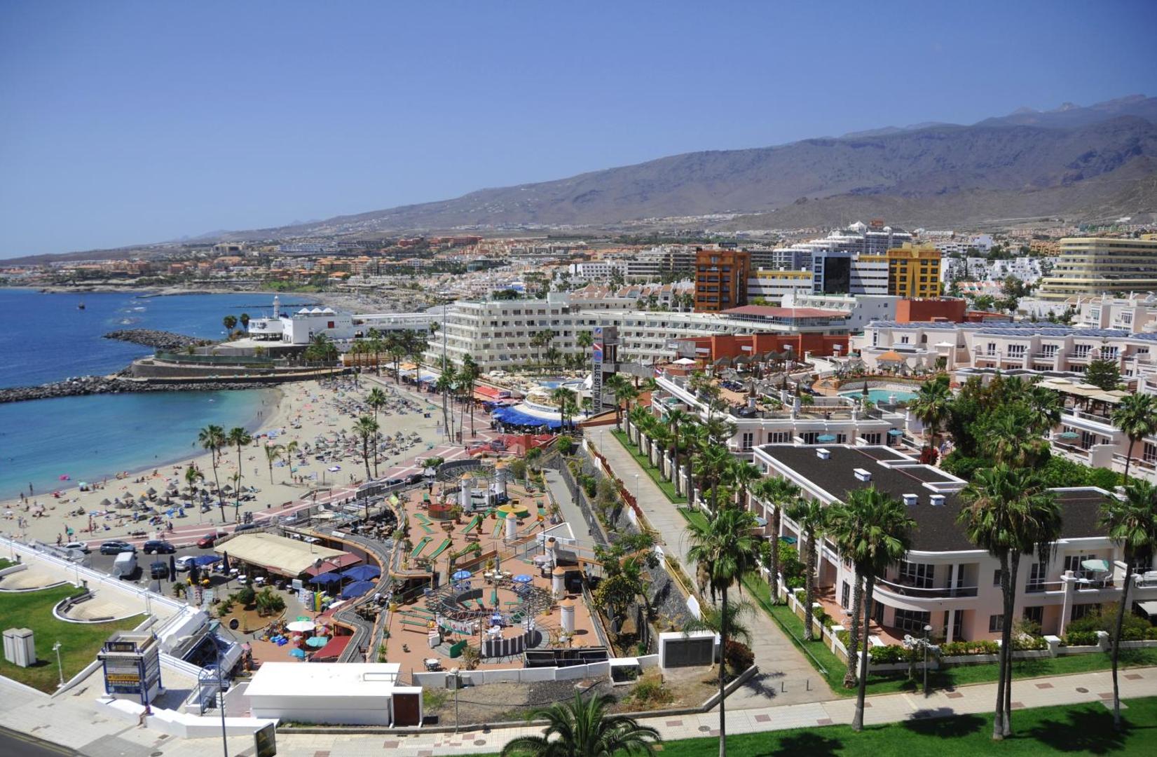 Panorāmas skats no Hovima Atlantis uz Tenerifes piekrasti, smilšu pludmali ar saulessargiem un apkārtējo pilsētas arhitektūru