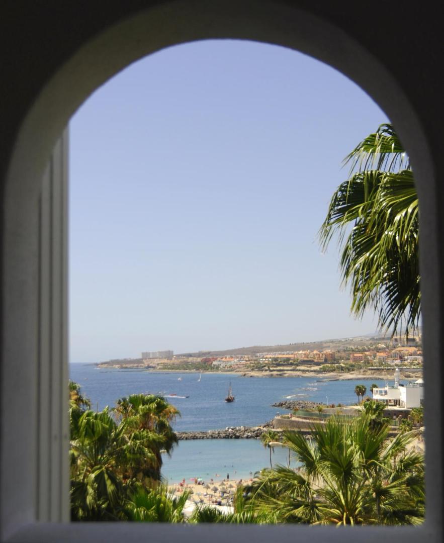 Skats no Hovima Atlantis viesnīcas arkas uz okeāna līci, pludmali un palmām Kostā Adehē, Tenerifē