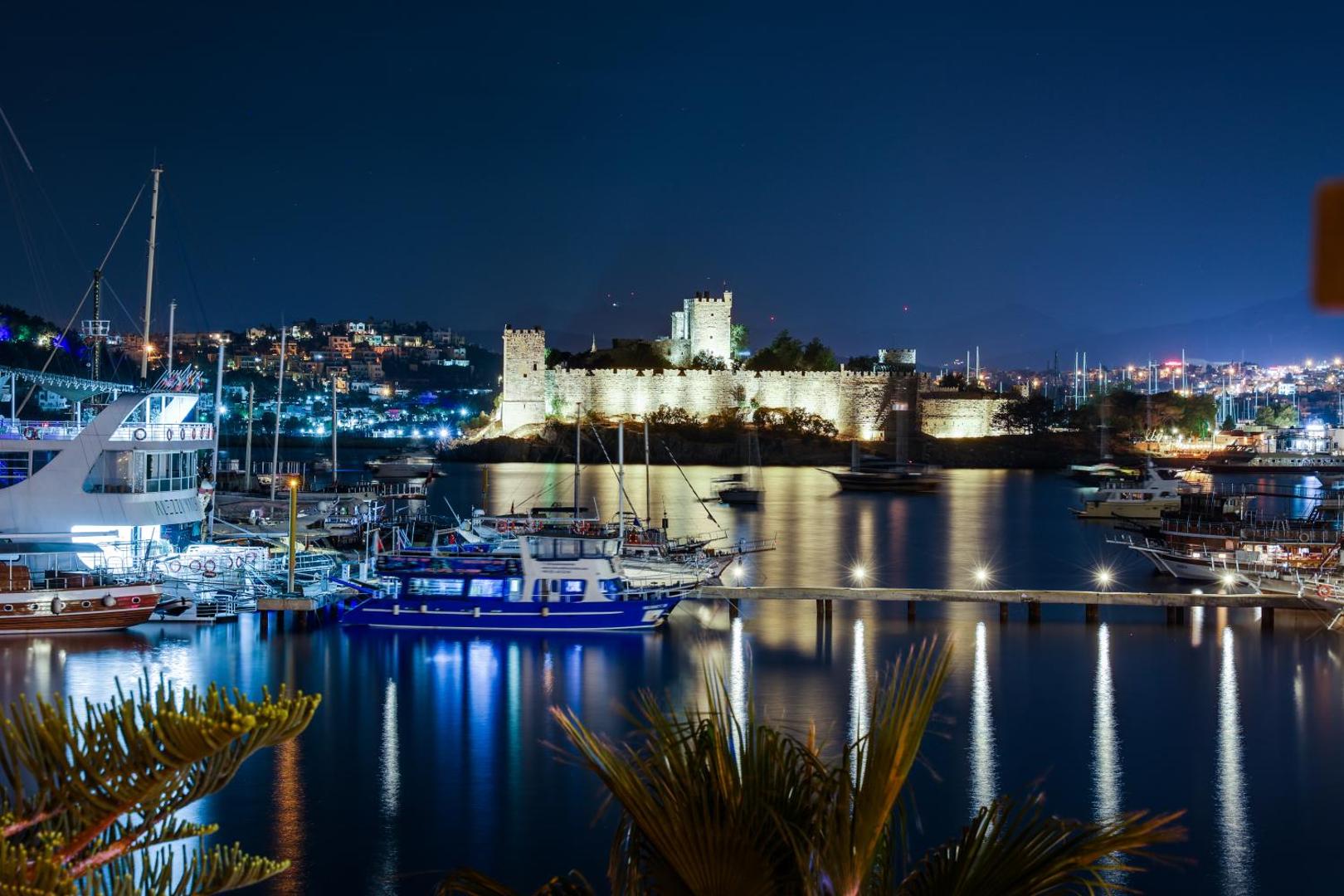 Diamond of Bodrum Hotel skats uz vēsturisko Bodrumas pili naktī no ostas puses ar pietauvotām laivām un pilsētas gaismām