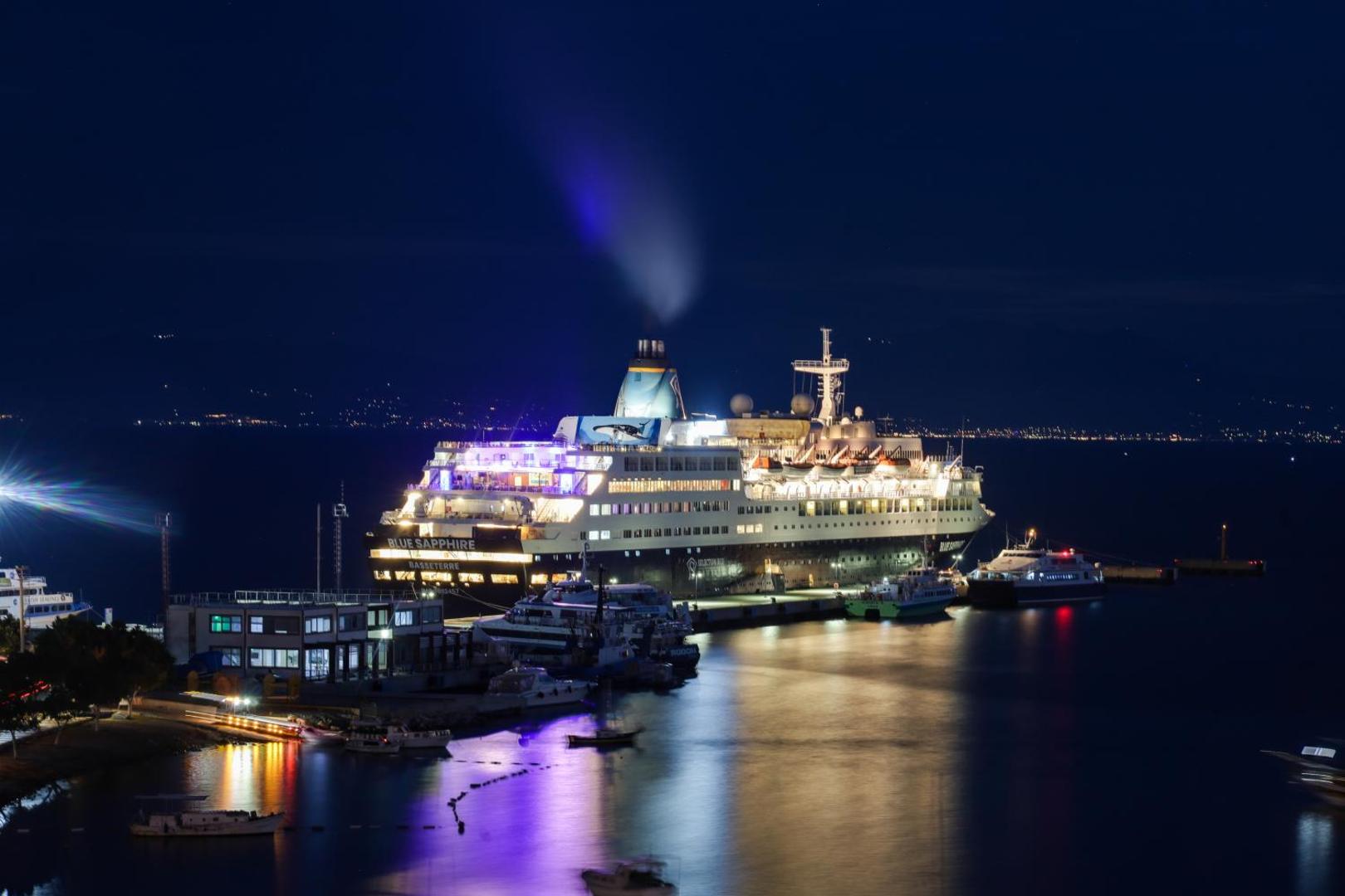 Liels kruīza kuģis Blue Sapphire piestātnē pie Diamond of Bodrum Hotel nakts laikā ar košām gaismām un atspulgiem ūdenī