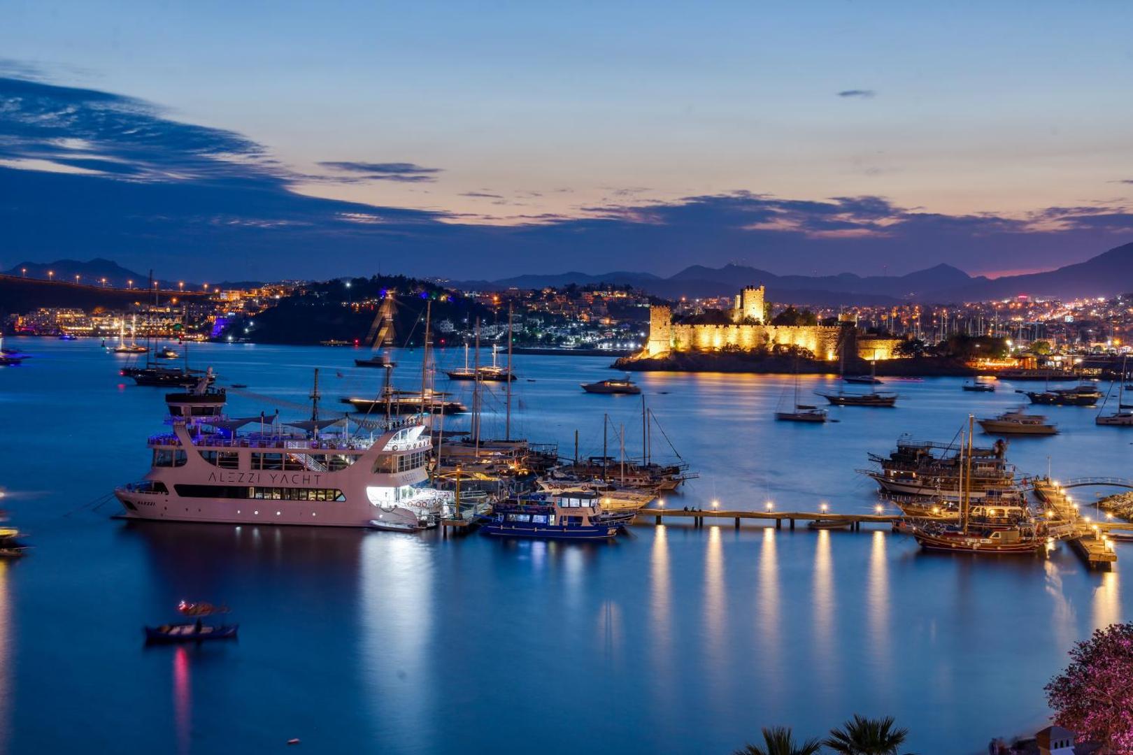 Diamond of Bodrum Hotel skats uz naksnīgo Bodrumas ostu un izgaismoto cietoksni Turcijā ar jahtām un kuteriem zilā ūdenī
