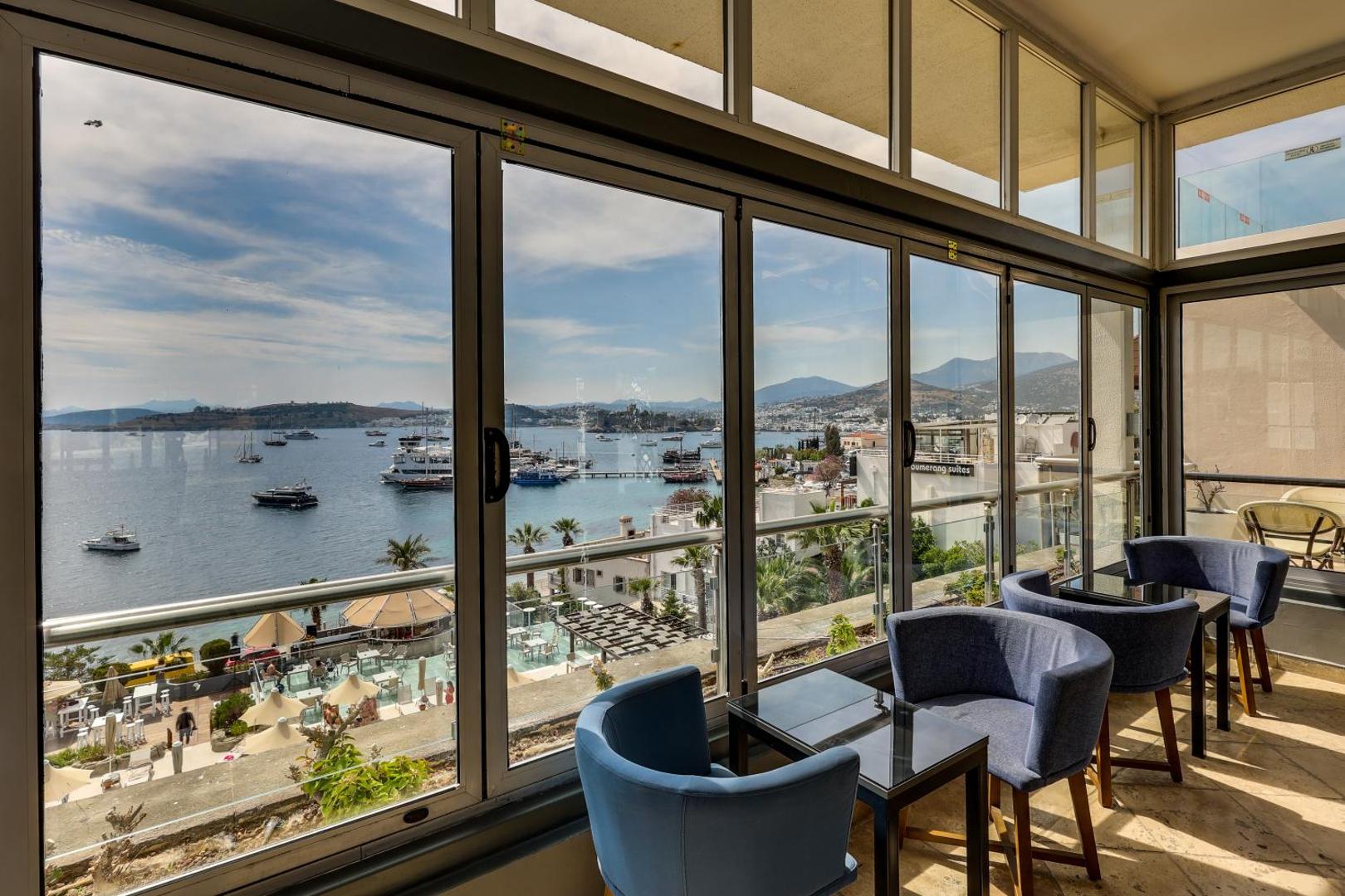 Diamond of Bodrum Hotel iestiklota atpūtas zona ar ziliem krēsliem un panorāmas skatu uz Egejas jūru un Bodrumas ostu