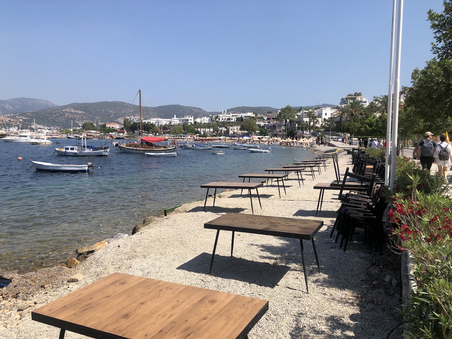 Diamond of Bodrum Hotel piekrastes zona ar galdiņiem tieši pie ūdens, skats uz Bodrumas līci un kalniem tālumā