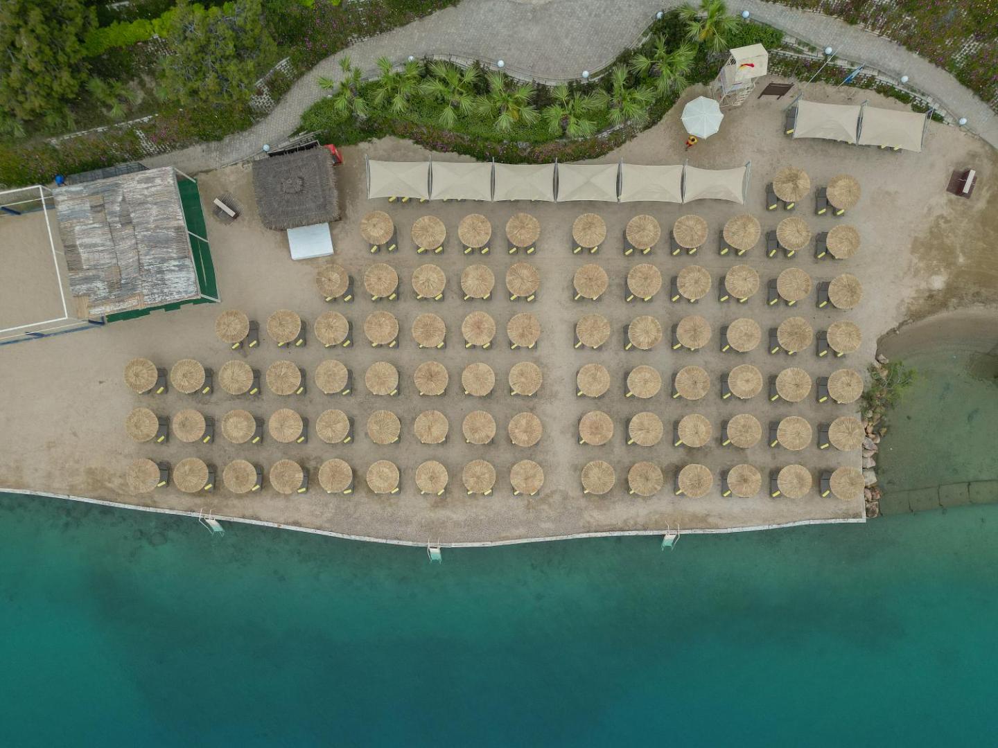 La Blanche Island Bodrum privātā pludmale no putna lidojuma — sakopti saulessargi un zviļņi pie dzidri zila Egejas jūras ūdens