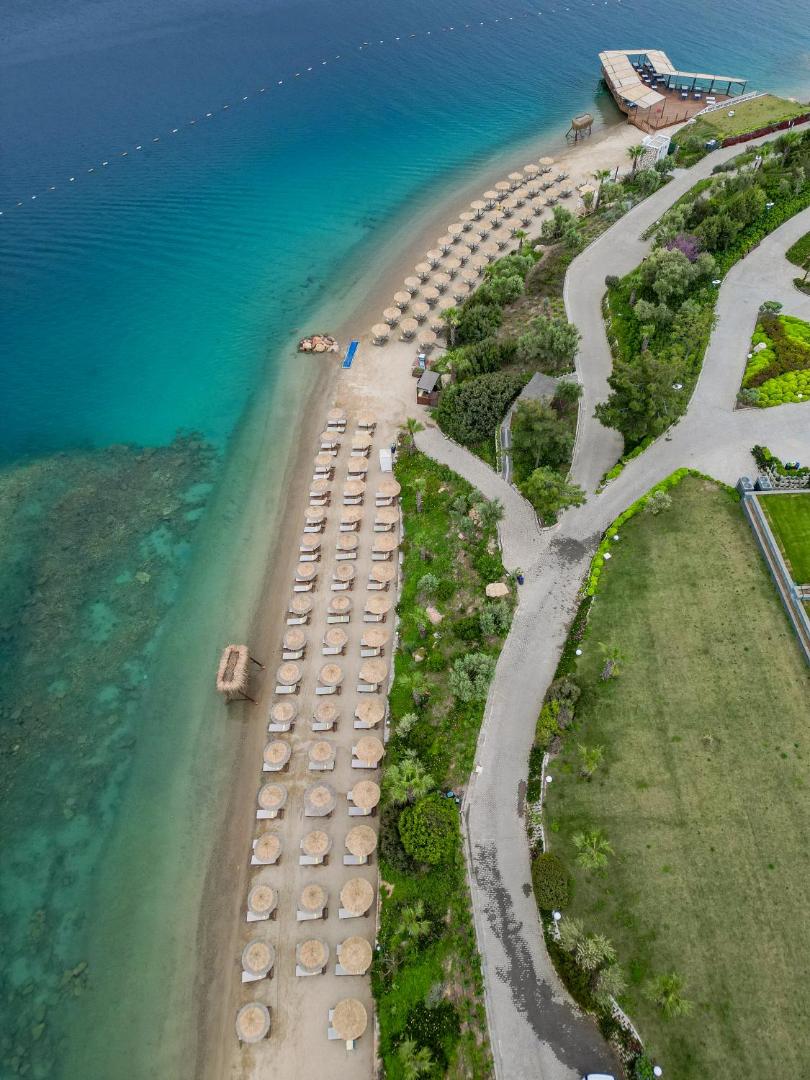 Skats no augšas uz La Blanche Island Bodrum piekrastes līniju, saulessargiem pludmalē, pastaigu takām un koptu zālienu