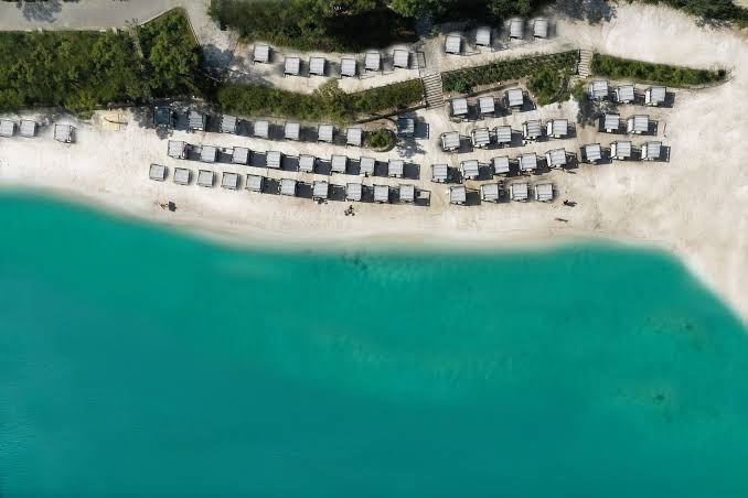 Aerofoto skats uz La Blanche Island Bodrum privāto pludmali ar baltām smiltīm, tirkīza ūdeni un rindu ar pludmales nojumēm