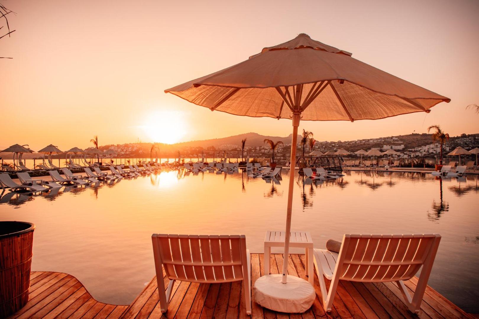 Saulriets pie Hotel Baia Bodrum bezgalības baseina ar sauļošanās krēsliem, saulessargiem un skatu uz kalniem un jūru