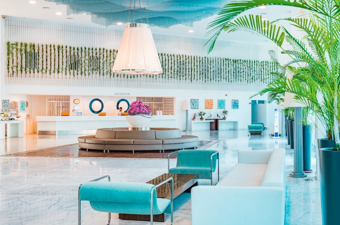 Hotel Baia Bodrum plašais un gaišais vestibils ar modernām mēbelēm, palmām un recepcijas zonu Bodrumā, Turcijā