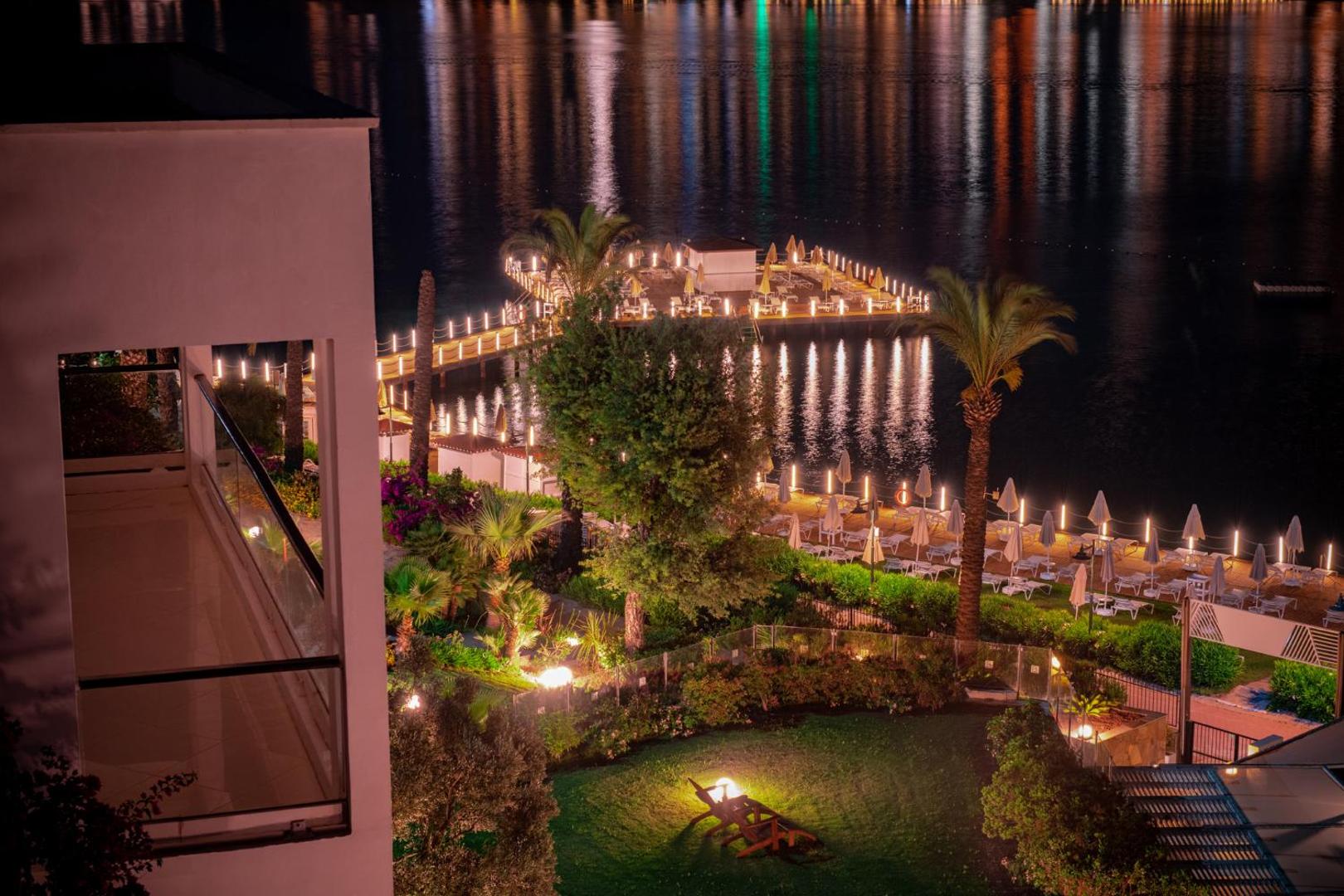 Hotel Baia Bodrum skats naktī uz izgaismotu koka piestātni, dārzu un jūras līci Bodrumas reģionā Turcijā