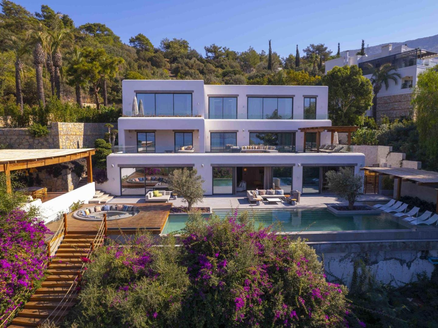 Rixos Premium Bodrum trīsstāvu villa ar baseinu, atpūtas zonu un ziedošiem krūmiem piekrastes pakalnā