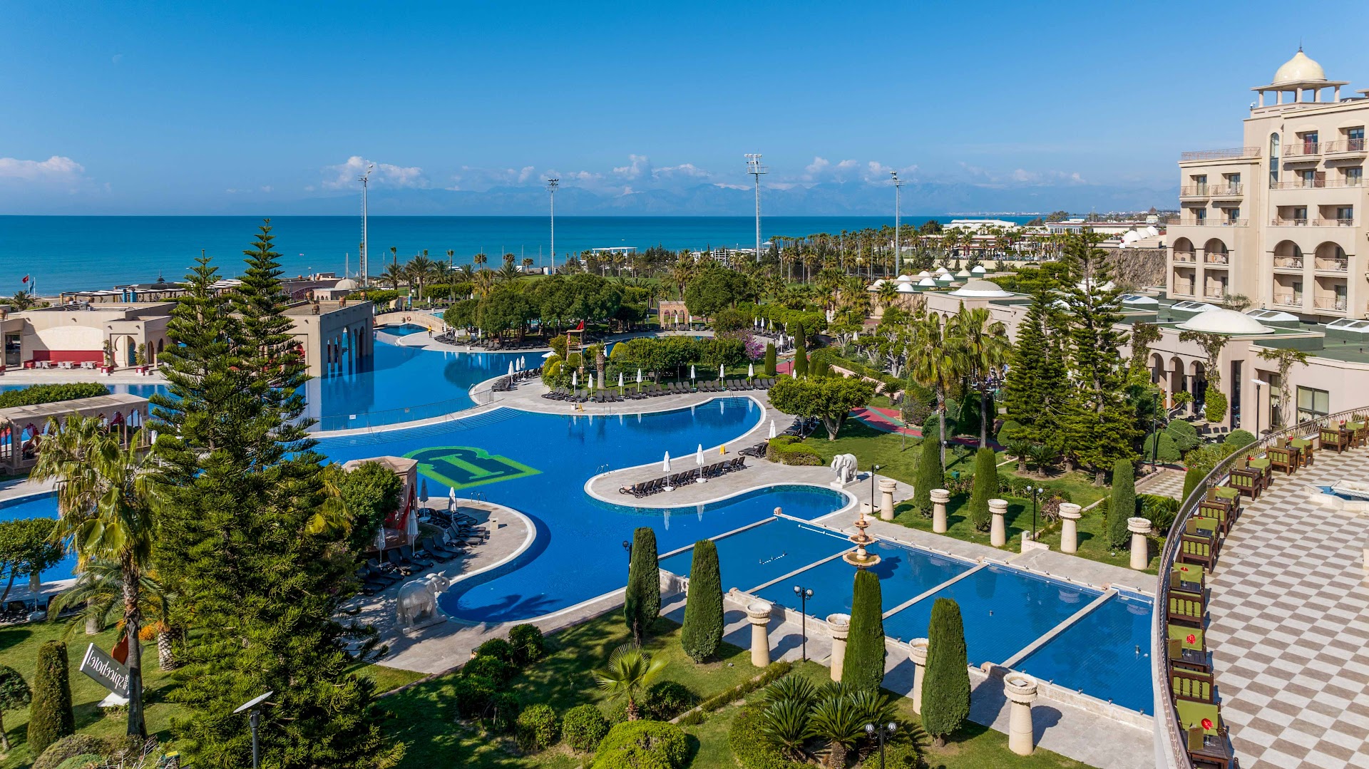 Spice Hotel & Spa galvenais āra baseins ar dekoratīvām kolonnām un ziloņiem, skats uz jūras horizontu un viesnīcas austrumu stila ēku.