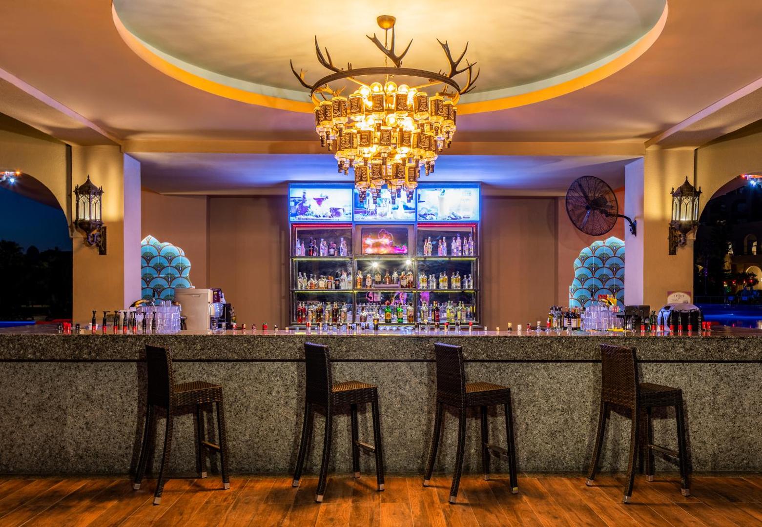Spice Hotel & Spa āra bāra lete vakarā ar modernu apgaismojumu, augstiem krēsliem un dekoratīvu lustru pie baseina
