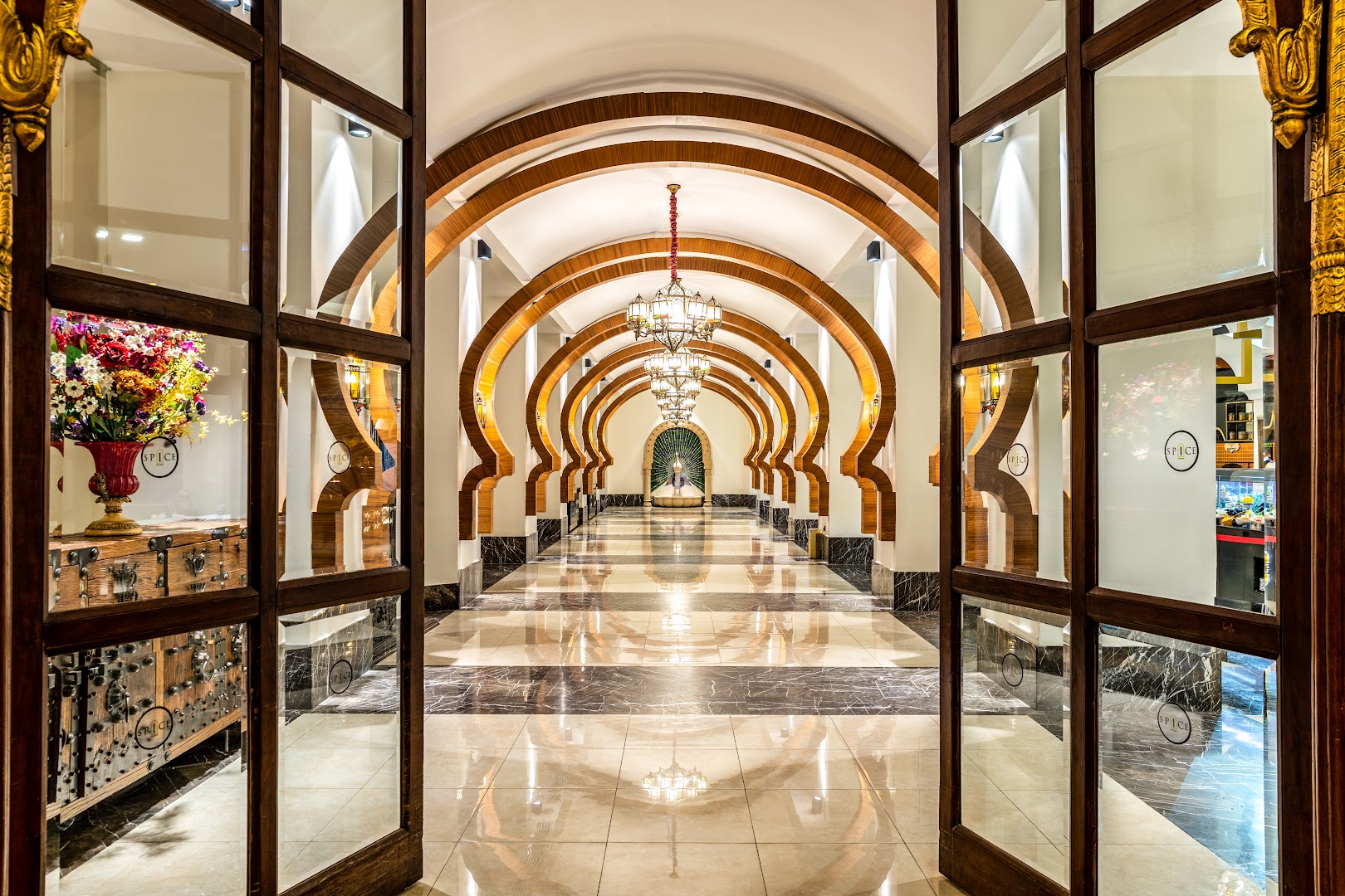 Spice Hotel & Spa viesnīcas gaitenis ar dekoratīvām koka arkām, marmora grīdu un greznām lustrām, kas ved uz restorānu zonu