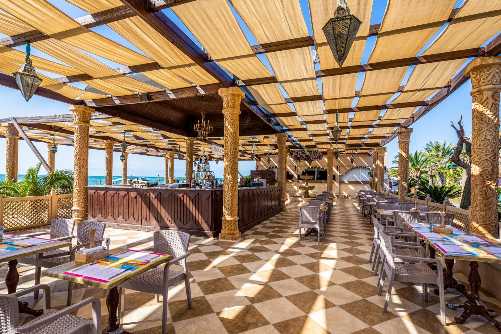 Spice Hotel & Spa āra bārs un restorāns Belekā ar austrumniecisku dizainu, koka kolonnām un nojumi saulainā dienā pie jūras