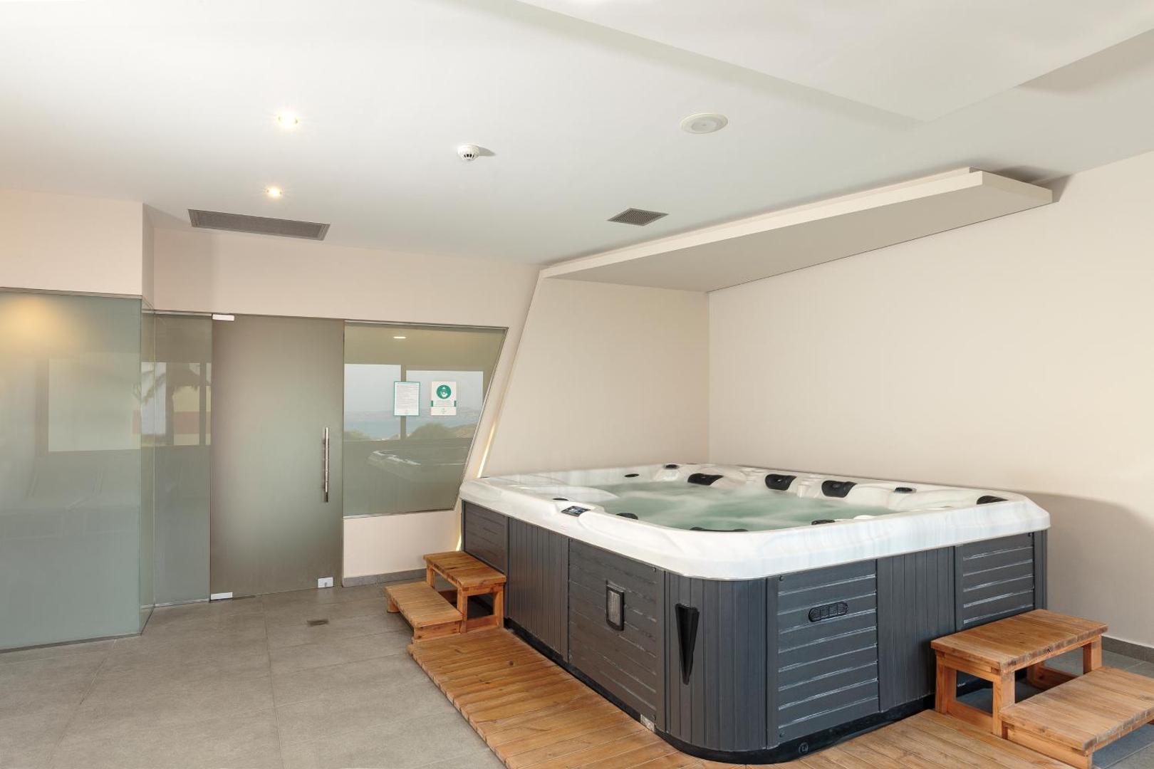 Iekštelpu džakuzi un spa zona Princess Sun Hotel viesnīcā Rodas salā ar koka pakāpieniem un modernu apgaismojumu