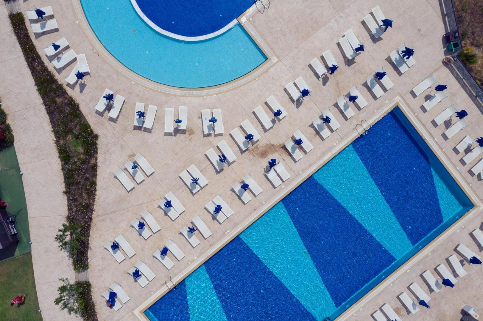 Princess Sun Hotel baseinu un sauļošanās zonas aerofoto Rodā — sakārtotas rindas ar krēsliem starp diviem dažādu formu baseiniem