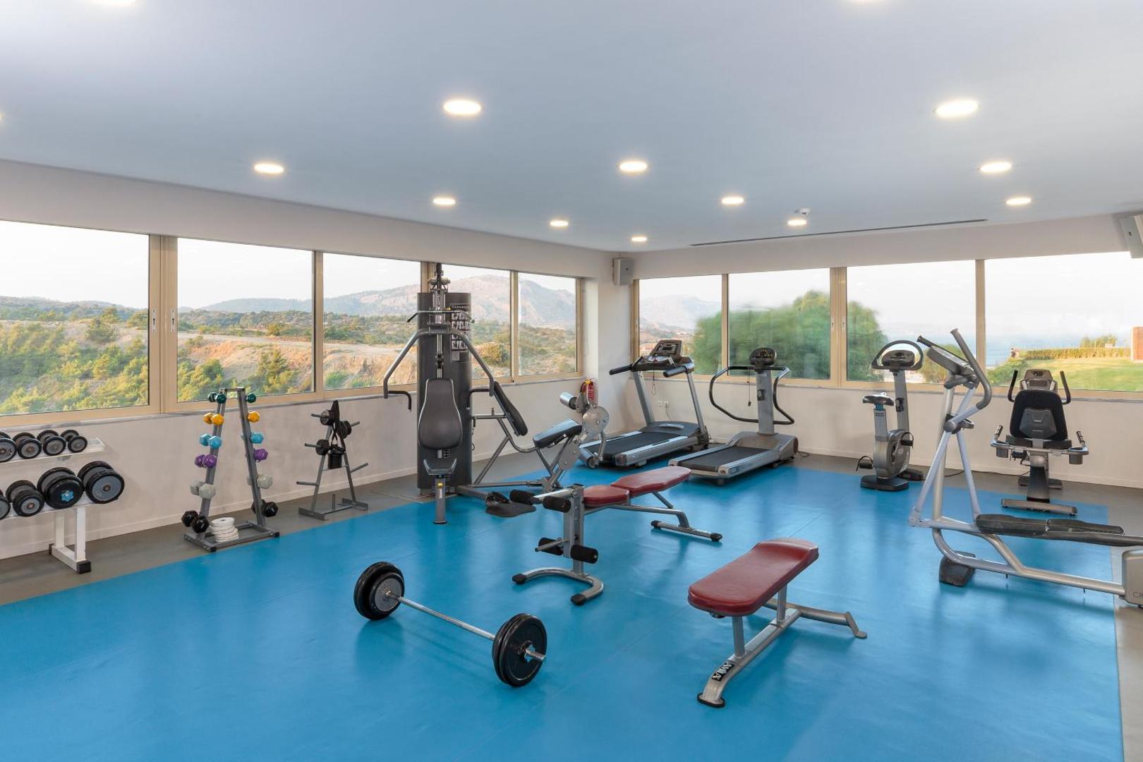 Princess Sun Hotel fitness centrs ar trenažieriem, svariem un lieliem logiem, pa kuriem paveras skats uz dabu