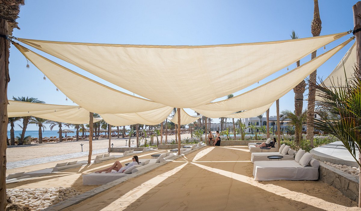 Serry Beach Resort atpūtas zona ar lielām saules burām, mīkstiem zviļņiem smiltīs un skatu uz jūru Hurgadas piekrastē.