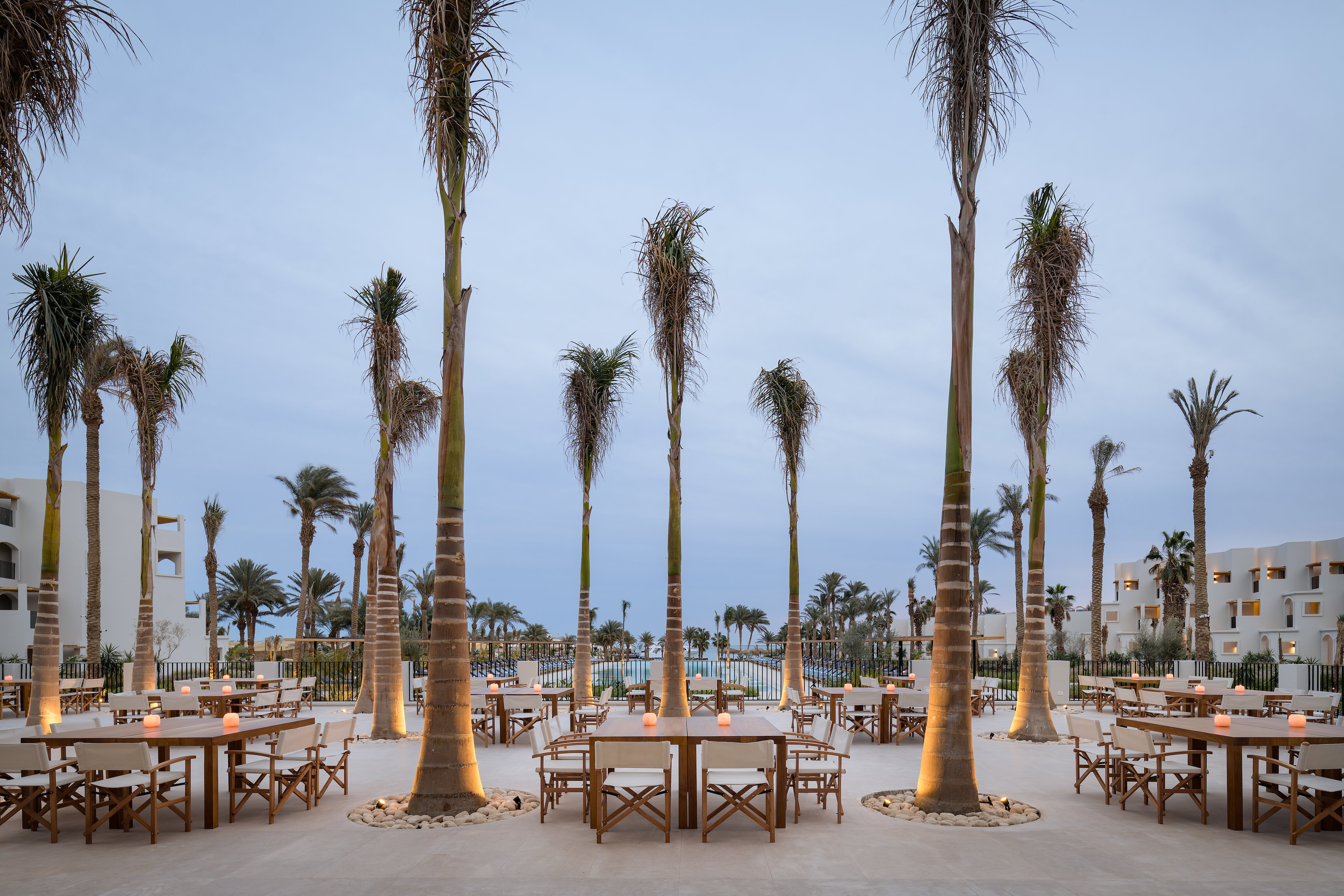 Serry Beach Resort āra restorāna terase vakarā ar izgaismotām palmām, koka galdiem un modernu arhitektūru Hurgadā.